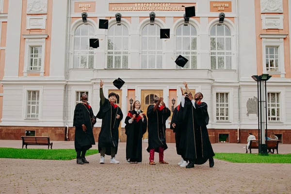 Graduates-group-in-gowns-celebrating-tossing-caps-outside-a-university-building